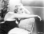 Bette Davis - Bette Davis sitting on the Couch while Smoking a Cigarette in Black Sleeveless Polka Dot Dress